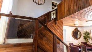 Una escala de fusta amb barana de vidre que condueix a un espai amb butaques de pell i un mirall a la paret.
