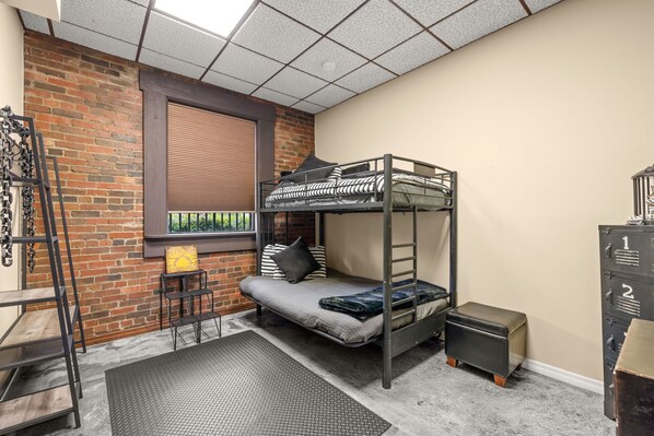 A bunk bed room with a brick wall, a window with blinds, a small table, and a metal cabinet. - Dade City's Historic 1892 Locke Inn Estate (Dade City)