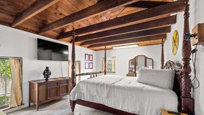 Un dormitori amb un llit amb cortines, bigues de fusta al sostre, televisió de pantalla plana, un aparador de fusta i una finestra gran amb cortines.