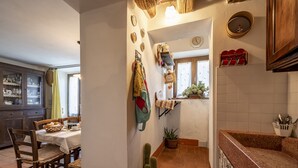 Une cuisine avec une table à manger, des chaises, une plante en pot et un porte-manteau suspendu.