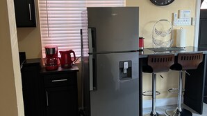 Une cuisine moderne équipée d’un réfrigérateur en acier inoxydable, d’une machine à café et d’une horloge murale.