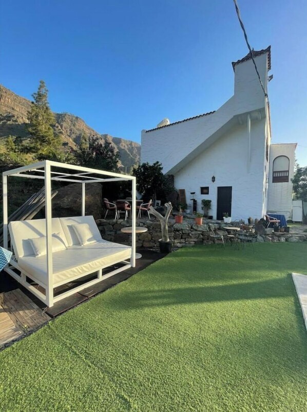 Una casa blanca con un muro de piedra y una cama con dosel blanco al frente.