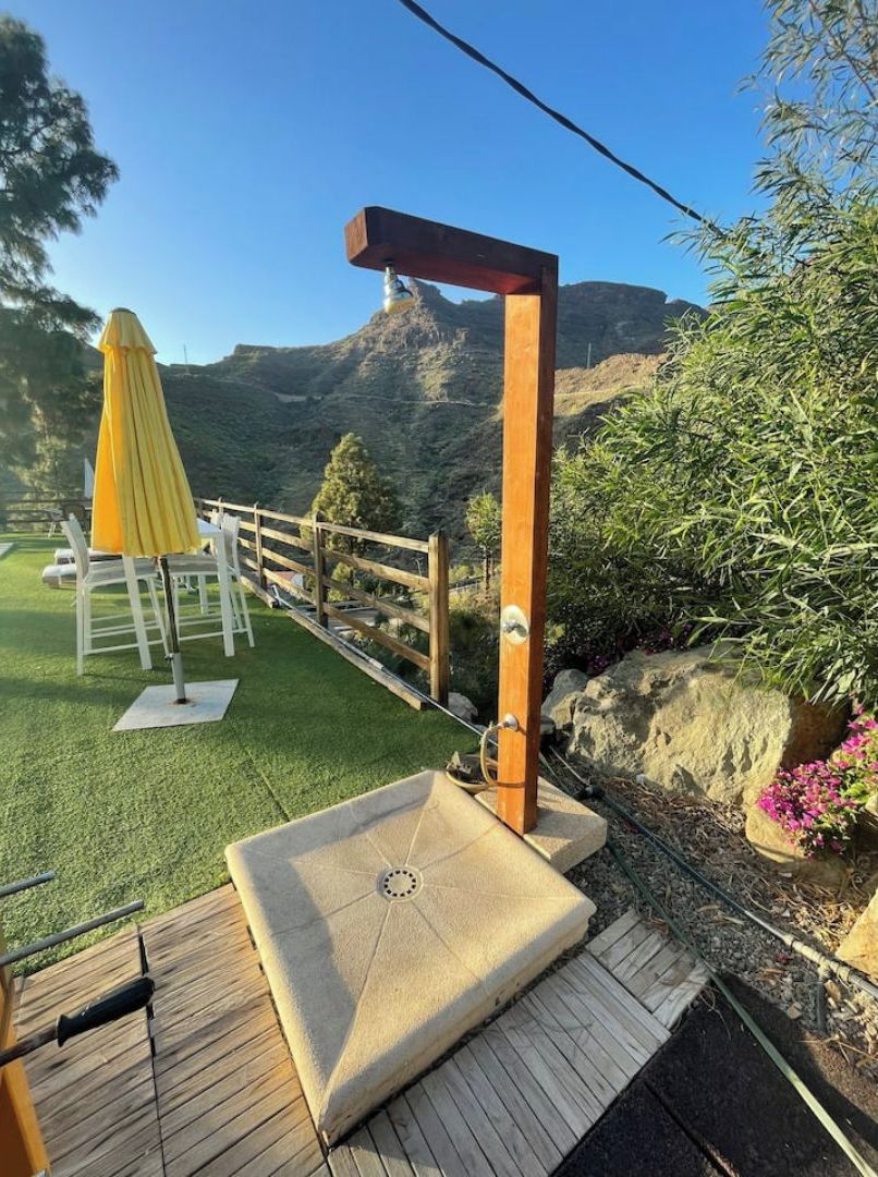 Une terrasse en bois avec un banc en pierre et un parasol jaune, offrant une vue sur un paysage montagneux.