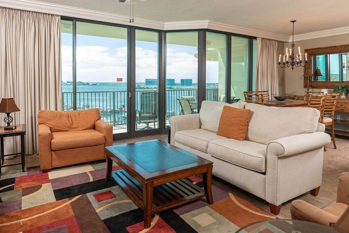 A spacious living room with a large window offering a view of the city and the sea, a sofa, a coffee table, and a dining area with chairs.