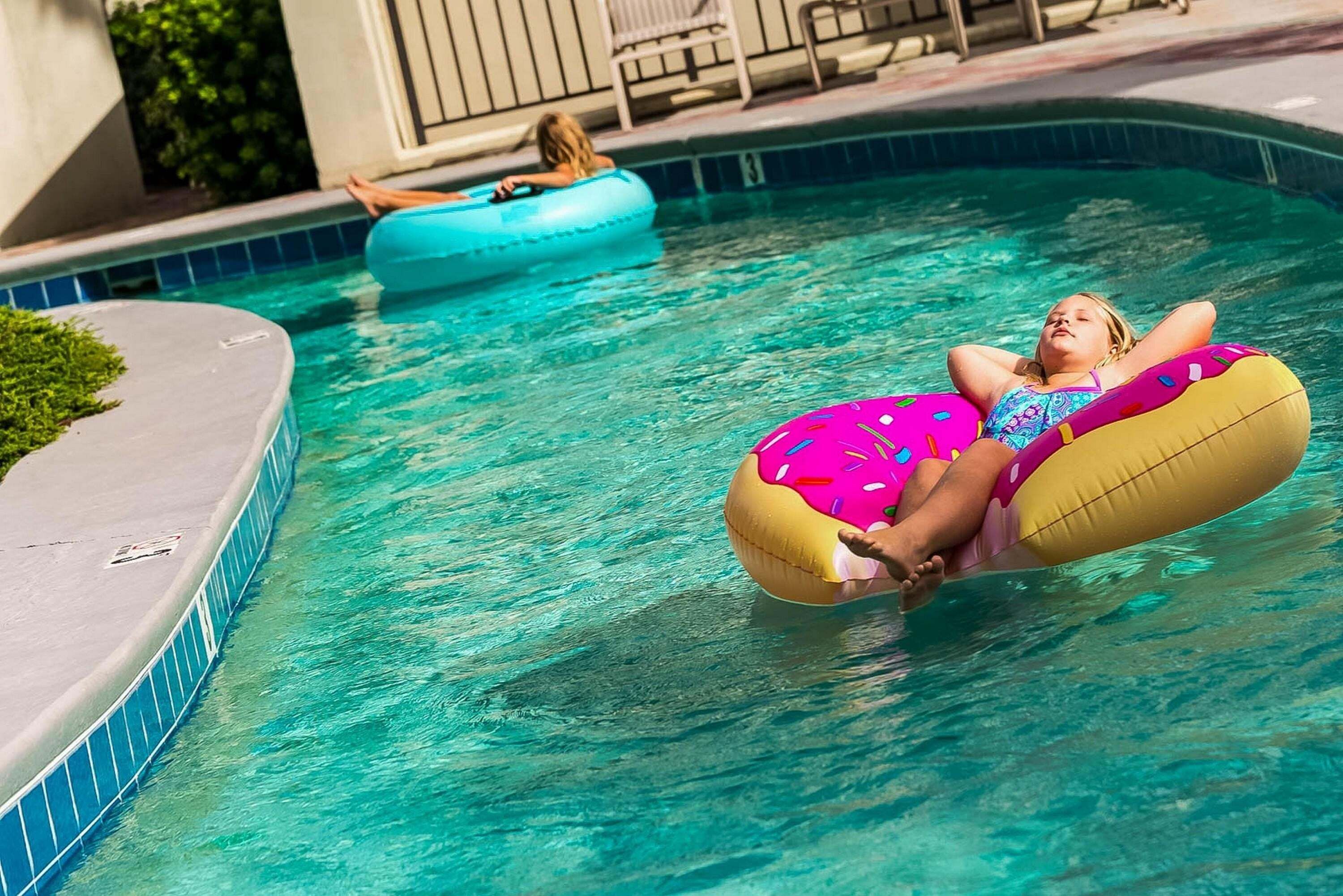 En swimmingpool med klart vand, flisekant og et loungeområde med stole.