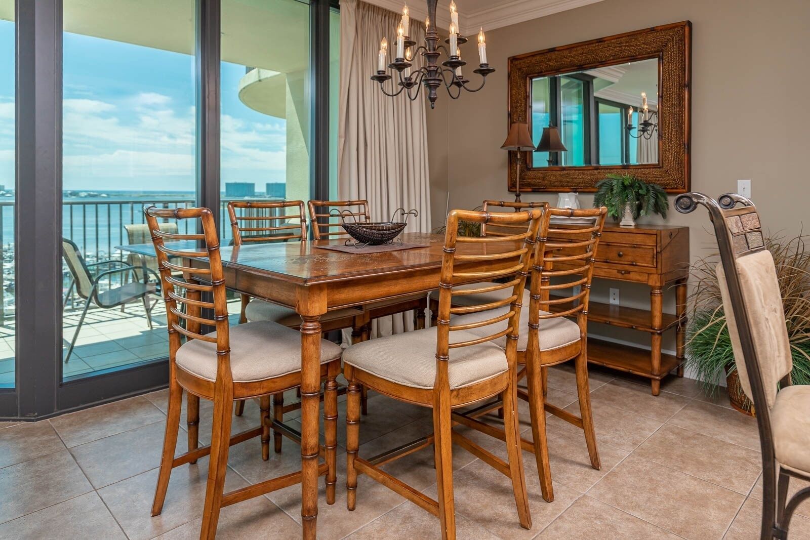 Un comedor con mesa y sillas de madera, una lámpara de araña, un espejo y vista al océano.