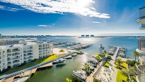 Un port de plaisance avec des bateaux amarrés, une promenade en bord de mer et un immeuble de grande hauteur doté de balcons donnant sur l’eau.