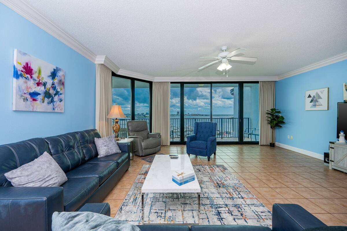 A spacious living room with a large window, a ceiling fan, and a view of the city.