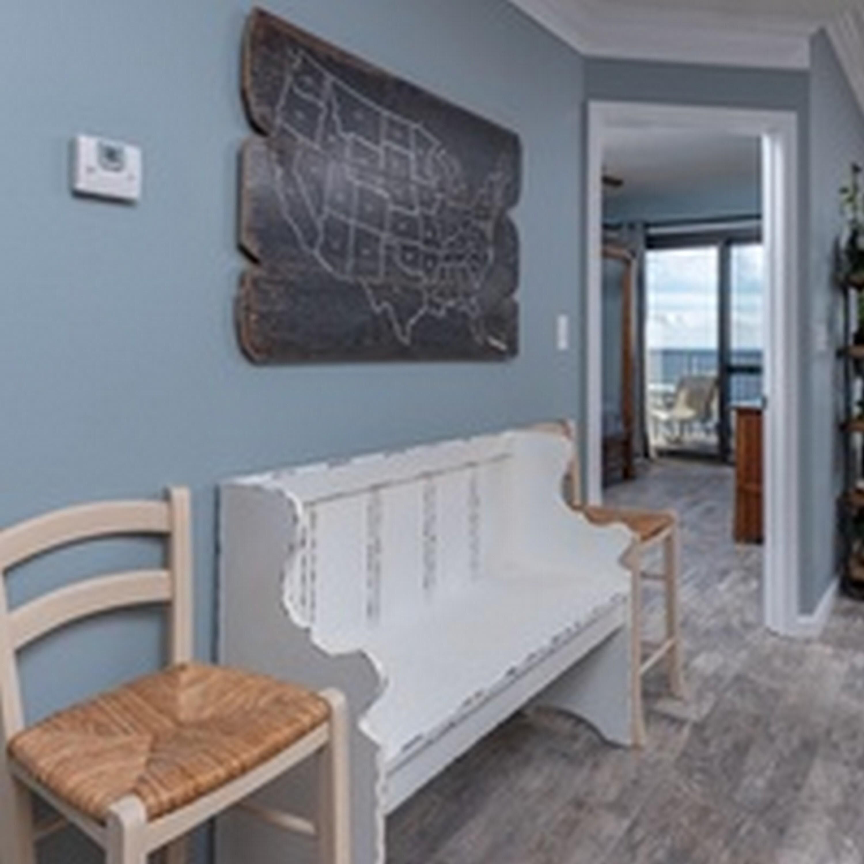 A room with a white bench, a wooden chair, and a wall map.