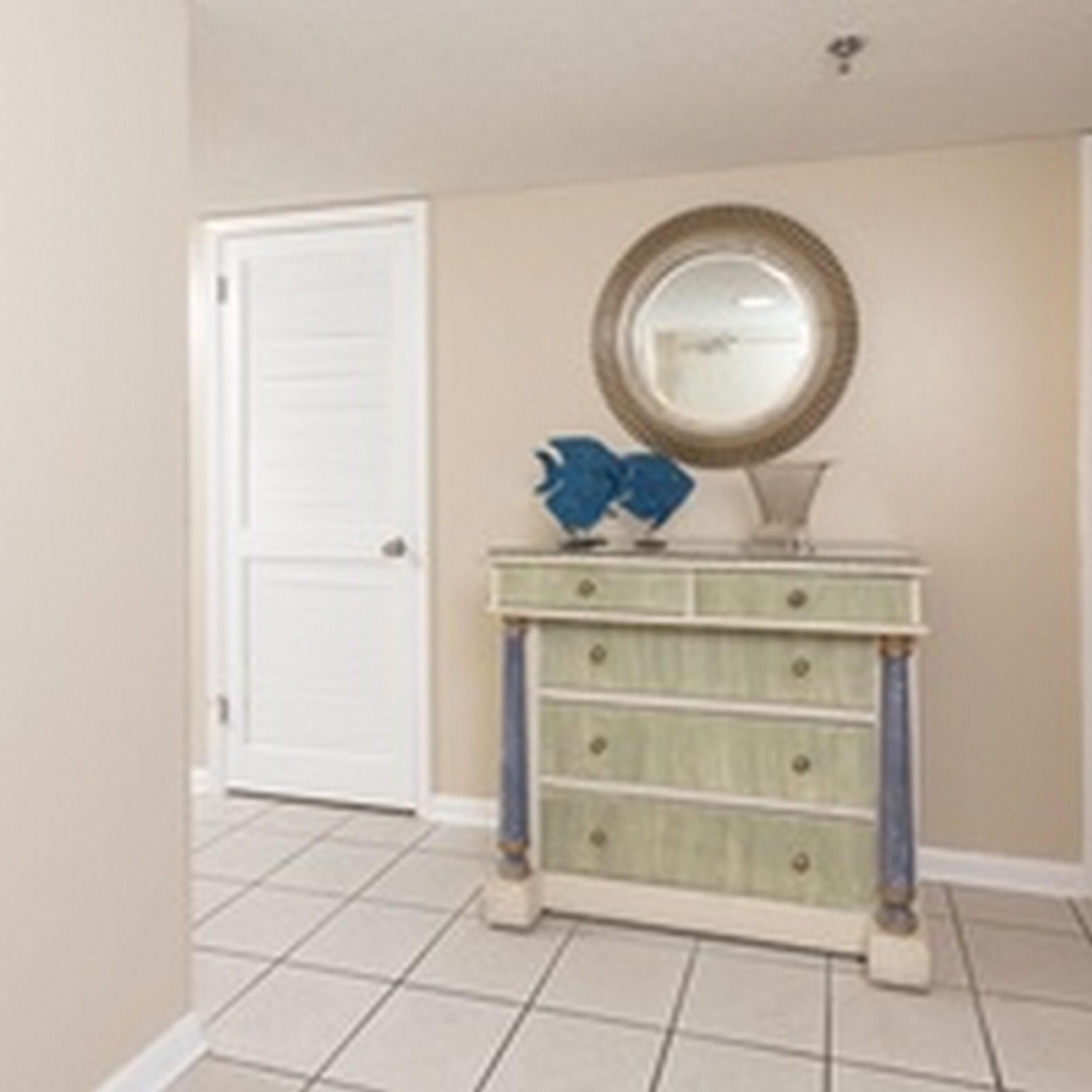 A room with a white door, a green vanity with drawers, a round mirror, and blue decorative items on the vanity.