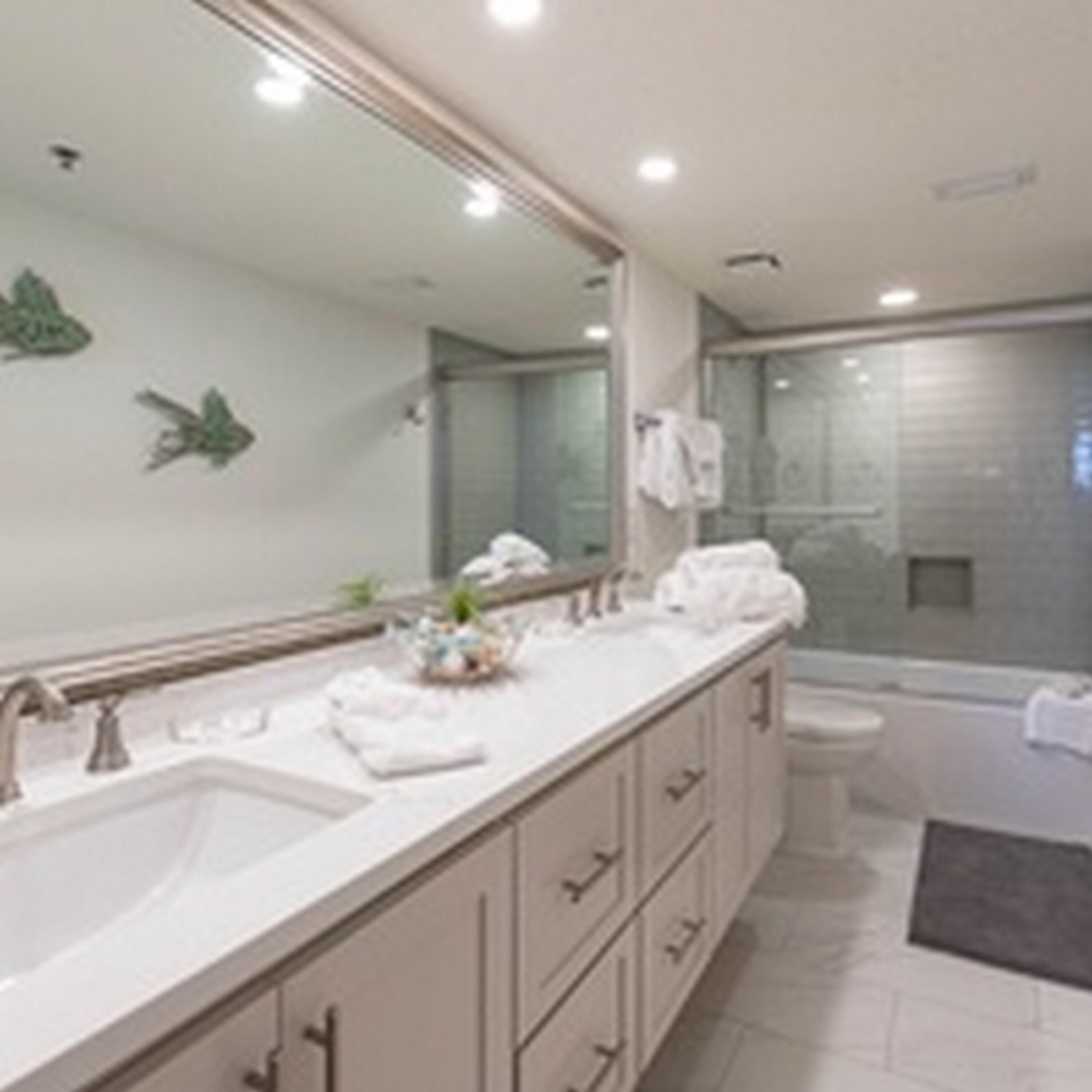 A modern bathroom with a large mirror, a sink, and a shower area.