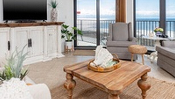 A spacious living room with a large flat-screen TV, a wooden coffee table, and a view of the ocean through large windows. - Phoenix VI by Brett Robinson Vacations (Orange Beach)