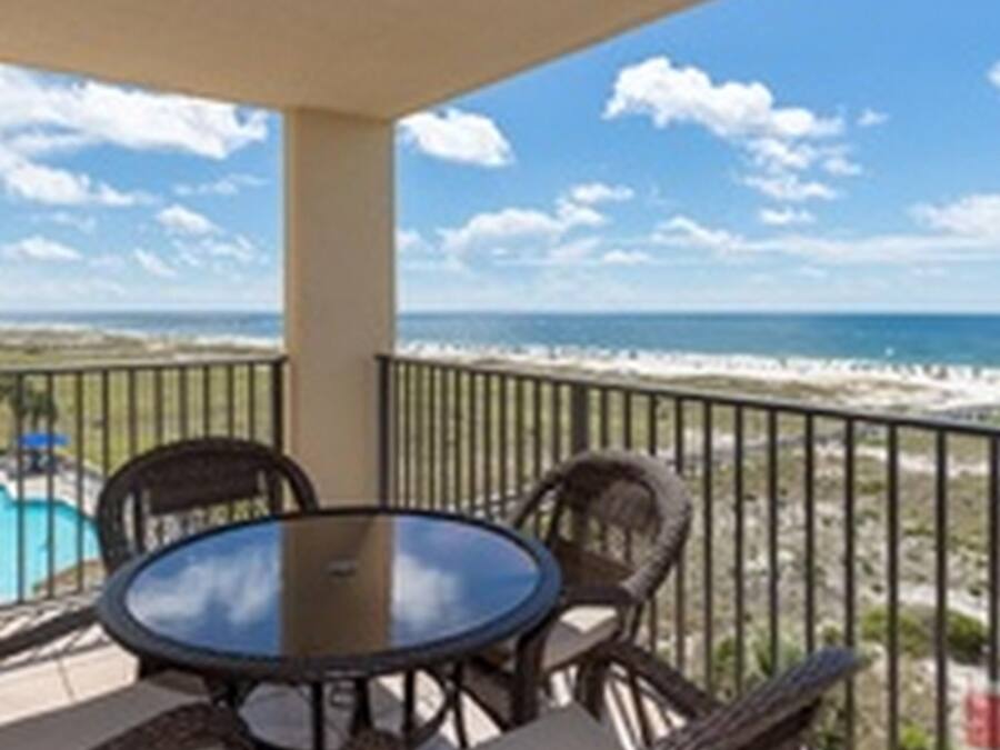 Ein Balkon mit rundem Tisch und Korbstühlen mit Blick auf einen Strand und den Ozean.