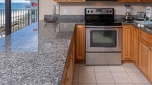 A kitchen with wooden cabinets, a stainless steel microwave, an oven, and a granite countertop. - Phoenix VI by Brett Robinson Vacations (Orange Beach)