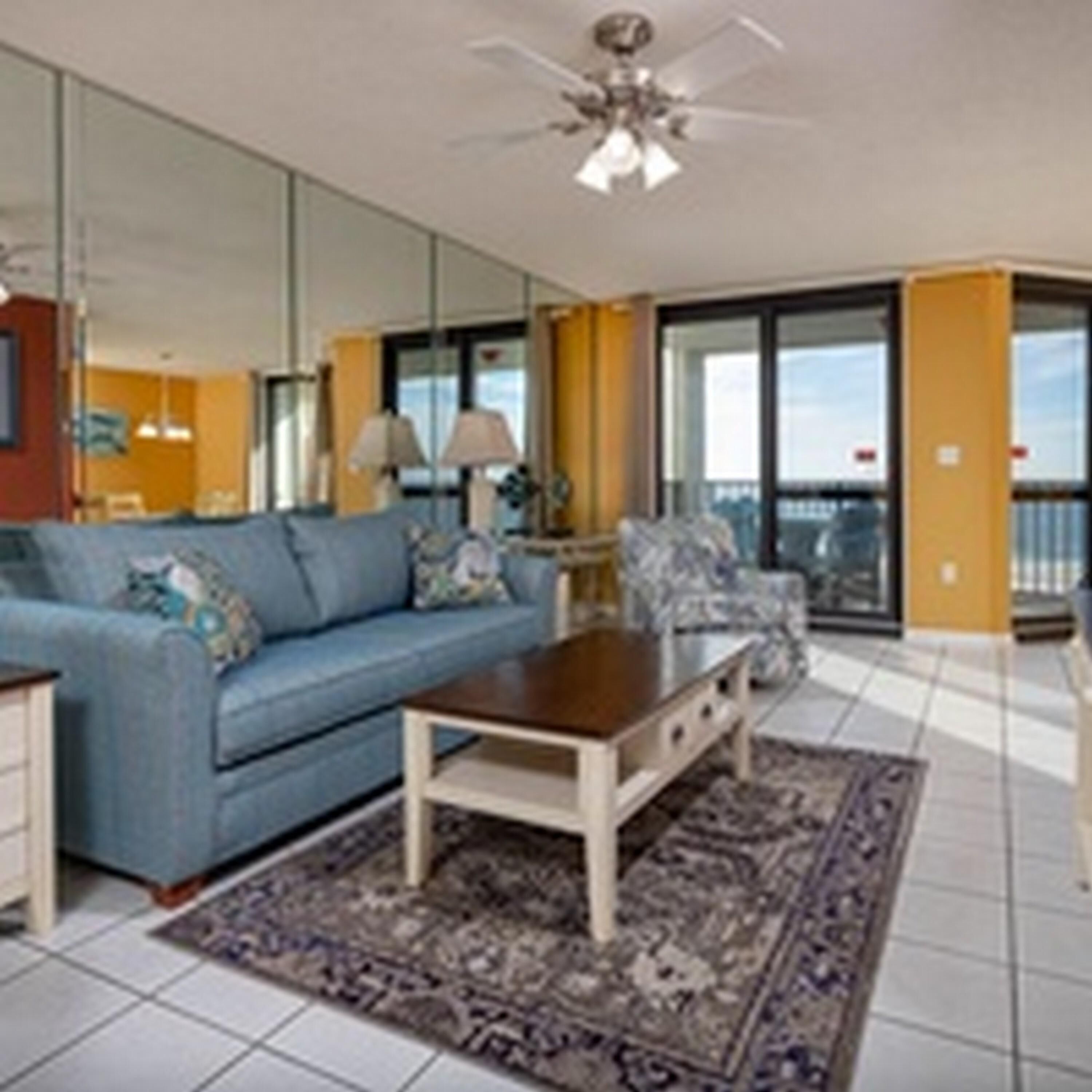 A living room with a blue sofa, a wooden coffee table, a patterned rug, and a ceiling fan.