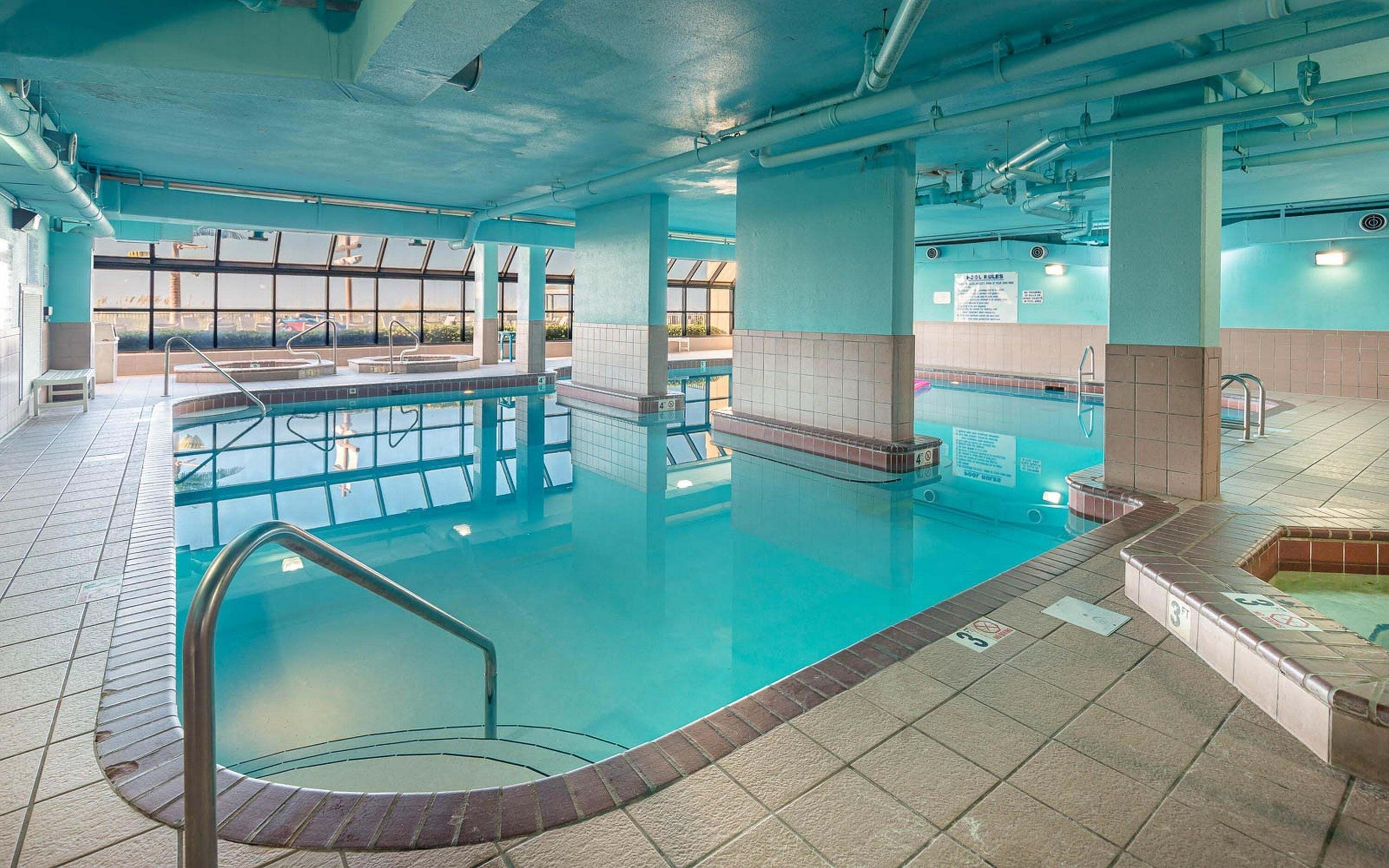 An indoor swimming pool with clear water, tiled floors, and visible poolside areas.