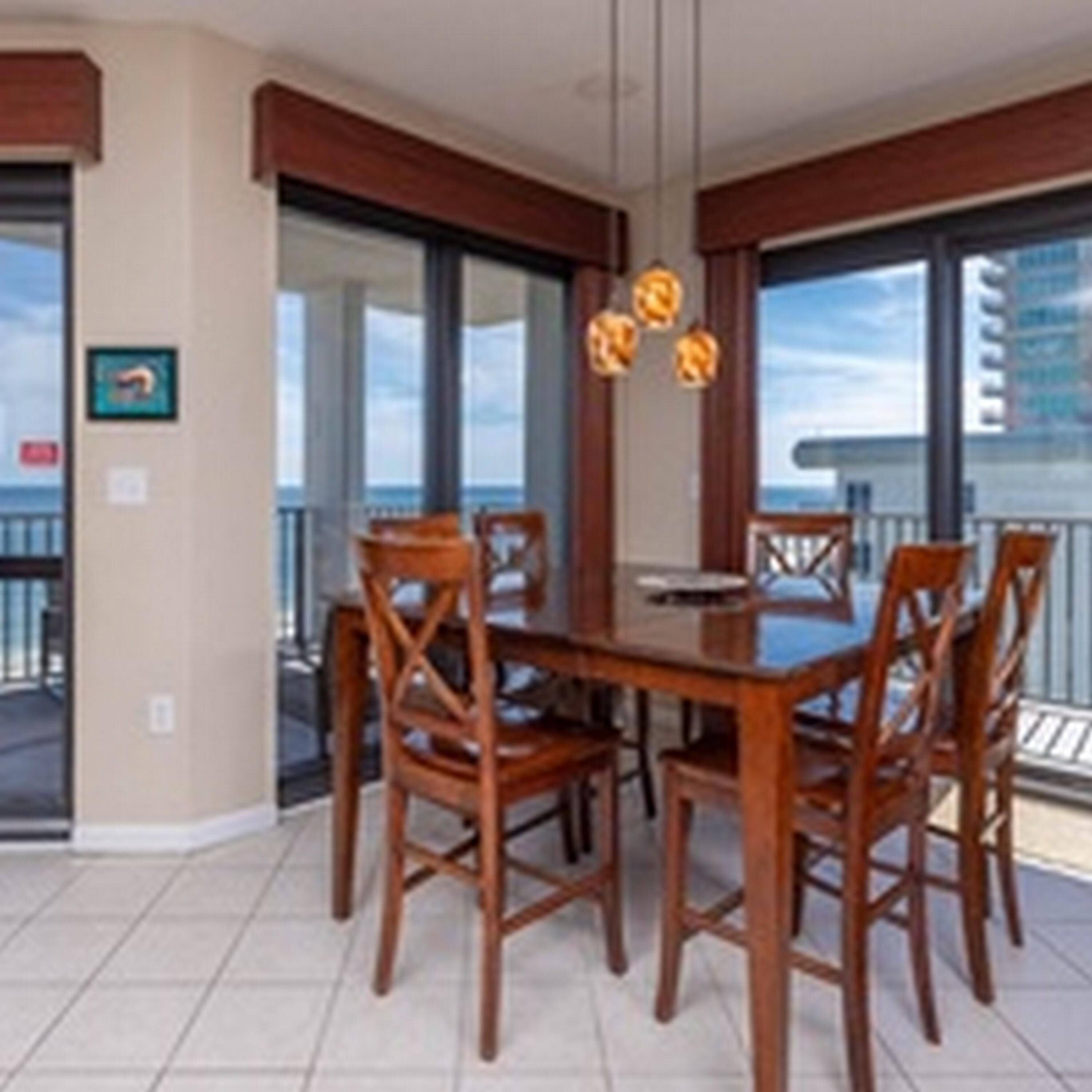 A dining area with a wooden table and chairs, large windows, and a view of the ocean.