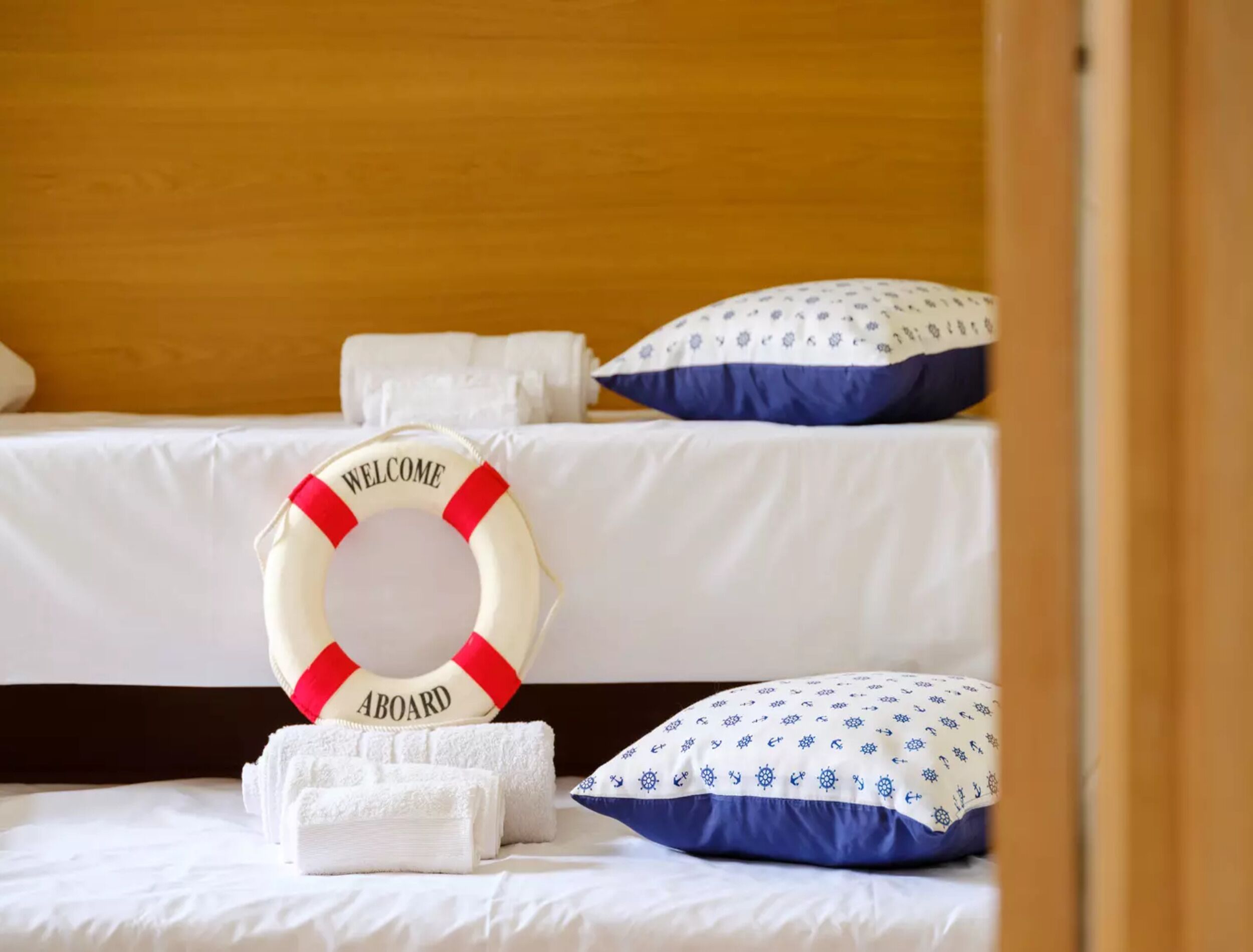 Ein Hotelzimmer mit einem Bett, einem Rettungsring mit dem Aufdruck 'WELCOME ABOARD', weißen Handtüchern und einem gemusterten Kopfkissen.