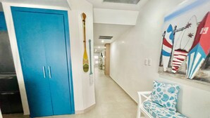 Un pasillo con una puerta azul, un banco blanco y un mural con pinturas de tablas de surf.