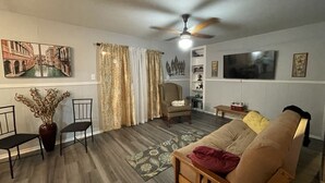 Ein Wohnzimmer mit einer Couch, Sesseln, einem Fernseher, einem Deckenventilator und einer dekorativen Vase.