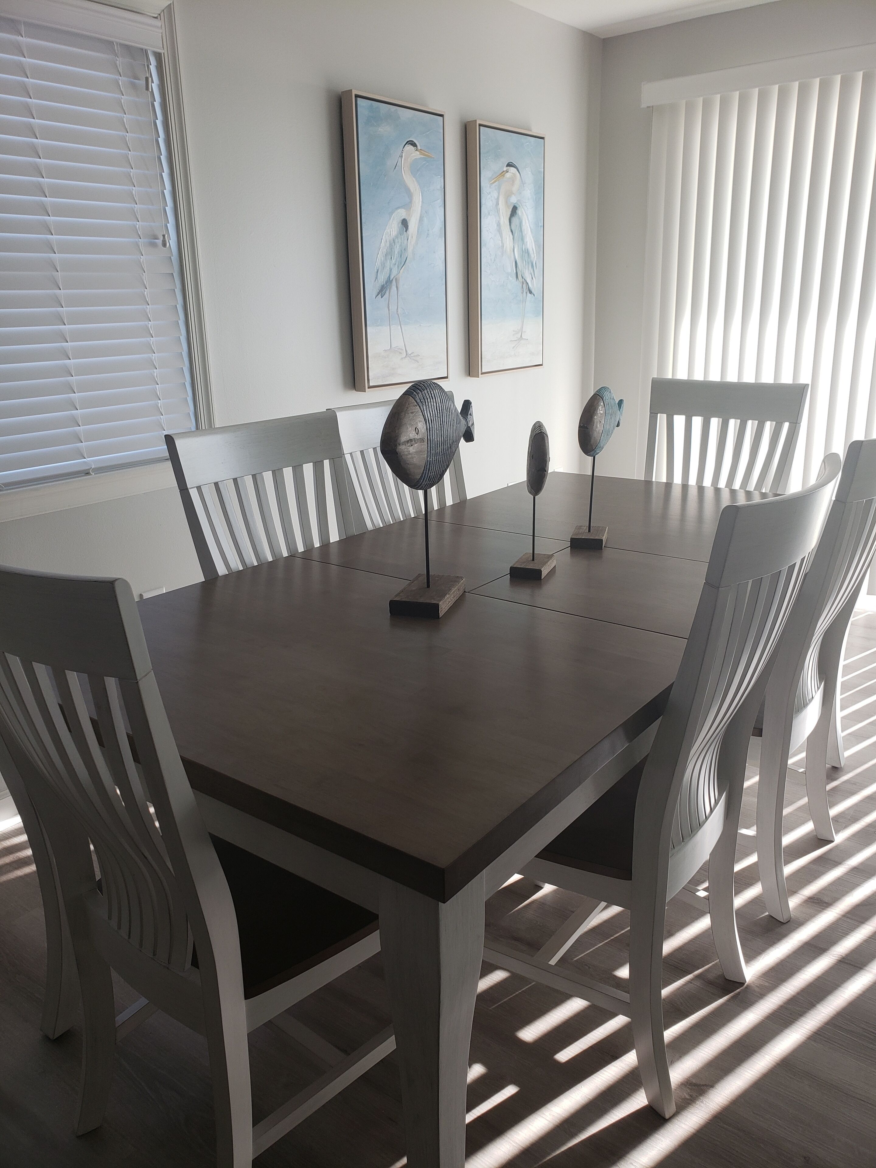 A dining area with a rectangular table, white chairs, and two wall-mounted fans.