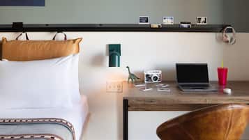 A hotel room with a bed, a desk with a laptop, a camera, and a red cup.