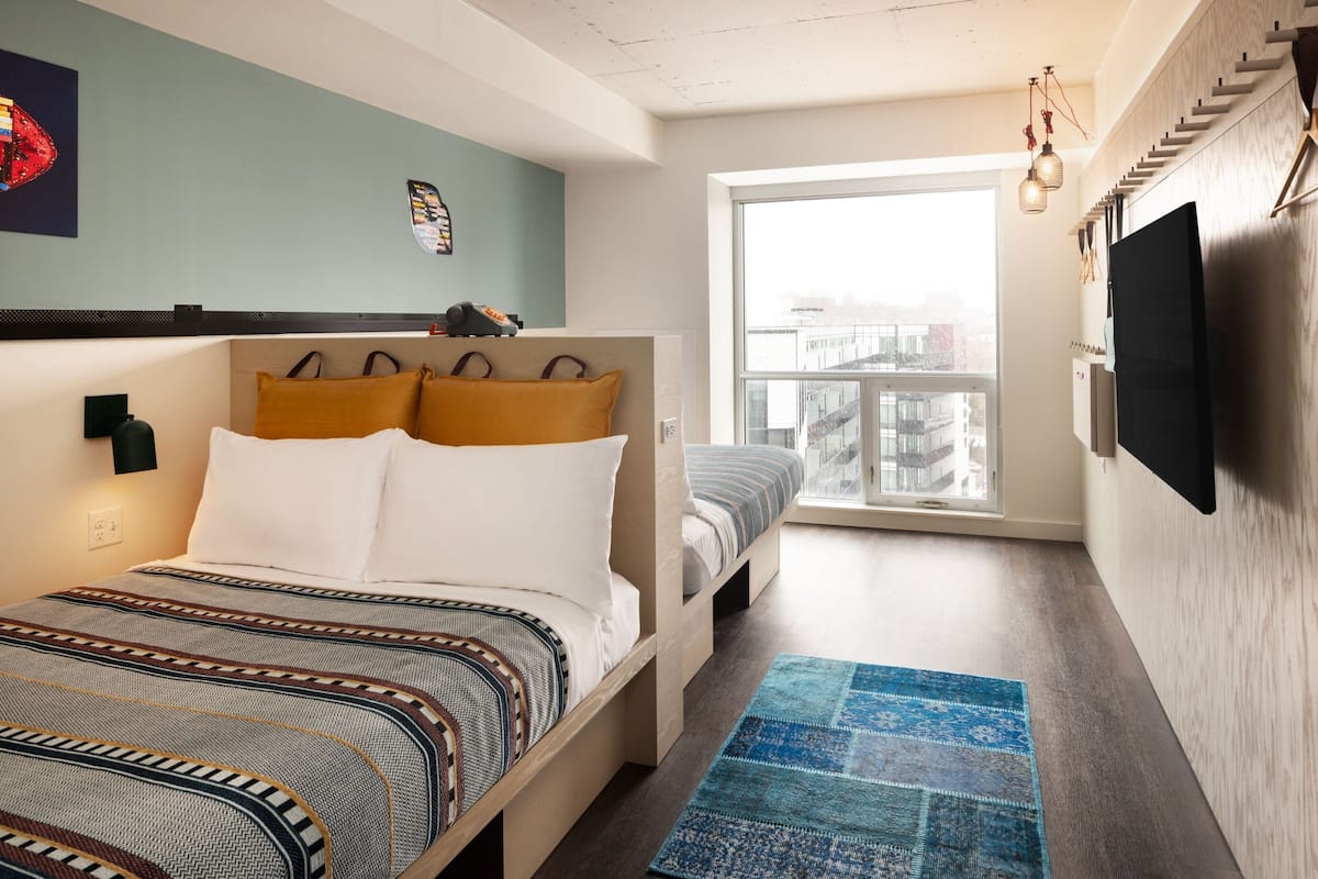 A bedroom with a bed, a small sofa, a window, and a TV.