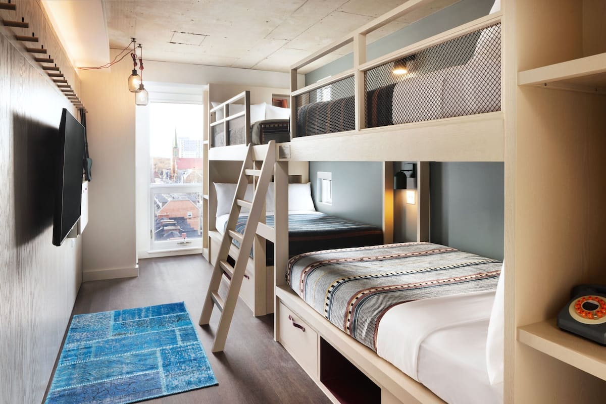 A bunk bed room with a TV, ladder, and a blue rug.