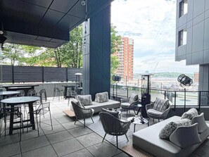 An outdoor seating area with tables and chairs, a sofa, and a view of a cityscape. - Moxy Halifax Downtown (Halifax)