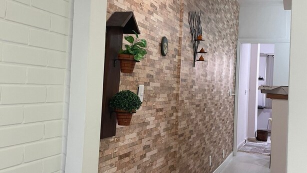Un couloir avec un mur décoré d’un motif en briques, une plante en pot, une horloge murale et un élément décoratif fixé au mur.