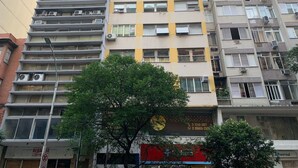 Un immeuble à plusieurs étages, doté de balcons, de climatiseurs et d’un arbre devant.