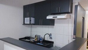Une cuisine de taille réduite, dotée de meubles de rangement sombres, d’un four à micro-ondes et d’un évier avec un robinet.