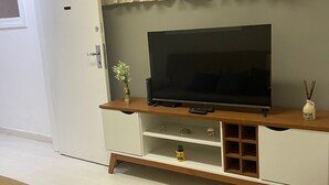 Un salon avec un téléviseur à écran plat posé sur un meuble télé en bois, un canapé beige et une porte blanche.