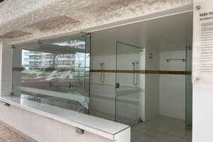 Un baño moderno con duchas de vidrio, un lavabo blanco y piso de baldosas.