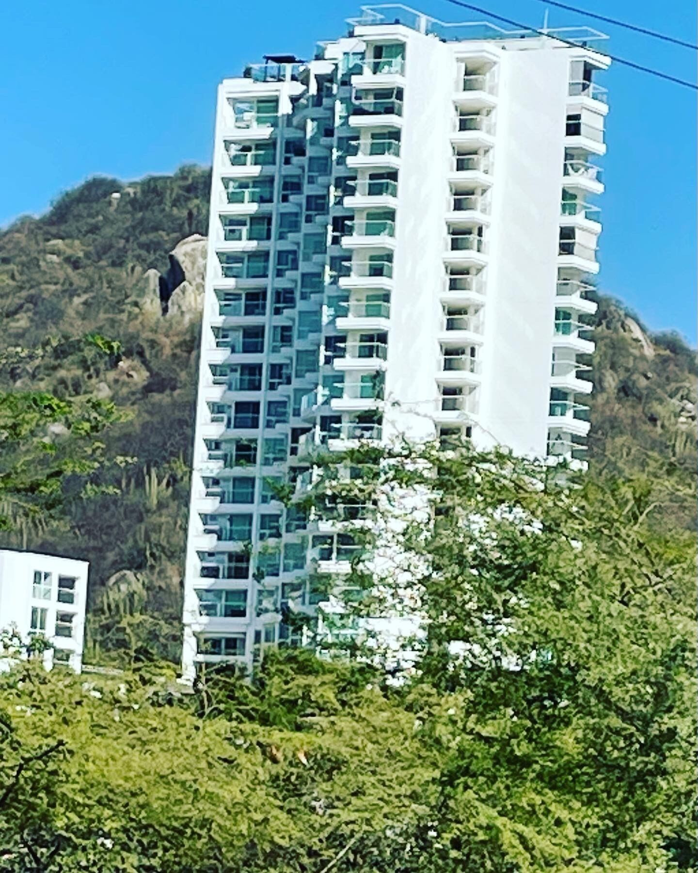 Edificio residencial de varios pisos con balcones, rodeado de vegetación y un paisaje montañoso.