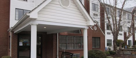A building with a covered entrance, a bench, and a small garden area.