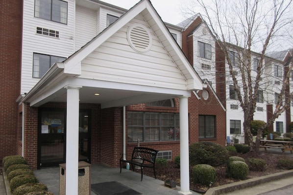 A building with a covered entrance, a bench, and a small garden area.