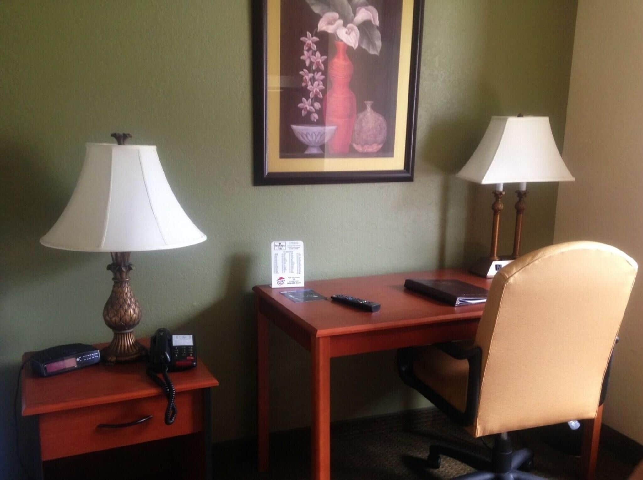 Une chambre d’hôtel équipée d’un bureau, de deux lampes, d’une chaise, d’un téléphone, d’une télécommande et d’un tableau encadré au mur.