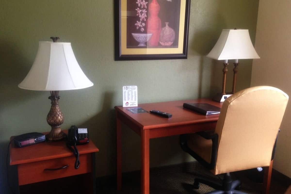 Une chambre d’hôtel équipée d’un bureau, de deux lampes, d’une chaise, d’un téléphone, d’une télécommande et d’un tableau encadré au mur.