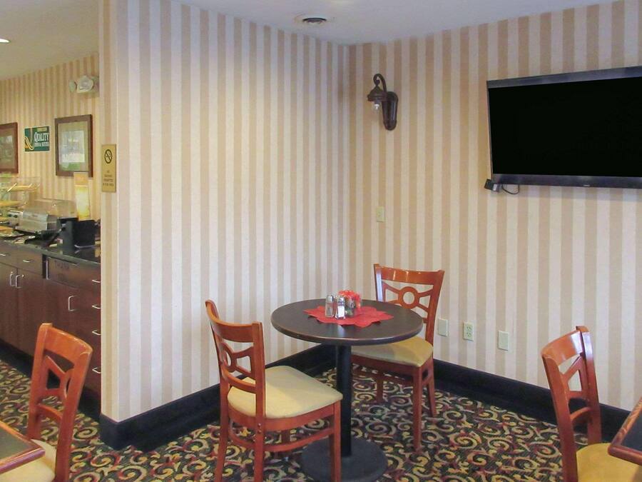 Uma área de refeições no canto, com papel de parede listrado, uma televisão na parede e um espaço de bar com eletrodomésticos.