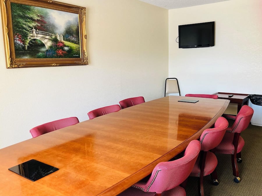 Un salón de conferencias con una larga mesa de madera, sillas tapizadas en rojo, un cuadro de un puente y un televisor de pantalla plana en la pared.