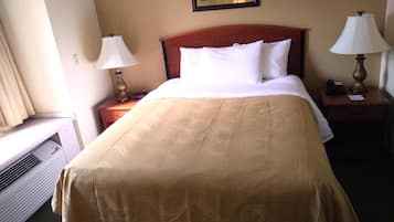 A hotel room with a bed, two bedside lamps, a nightstand, a heater, and a painting on the wall.
