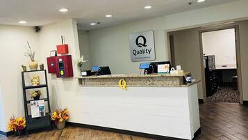 Una recepción de hotel con un cartel de 'Quality by Choice Hotels', un quiosco informativo rojo y un mostrador de recepción.