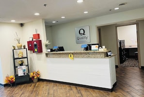 A hotel reception desk with a 'Quality by Choice Hotels' sign, a red information kiosk, and a reception counter.