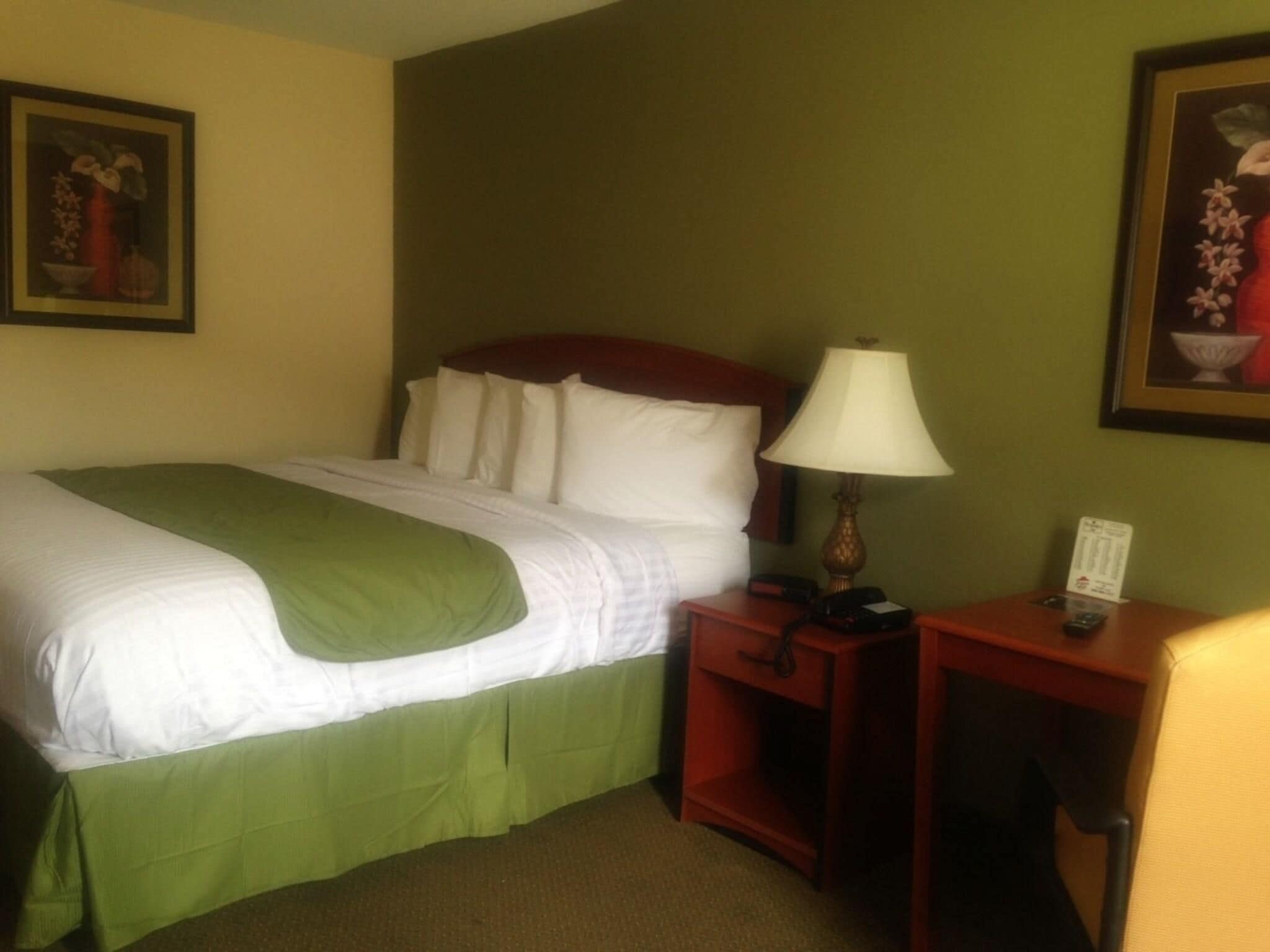 Habitación de hotel con cama, mesita de noche, lámpara y dos cuadros en las paredes.