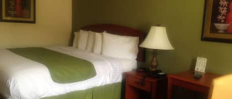 A hotel room with a bed, a nightstand, a lamp, and two framed pictures on the walls.