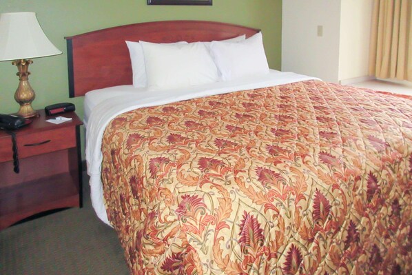 A hotel room with a large bed, a wooden headboard, a nightstand with a lamp, and a telephone. - Quality Inn & Suites Prestonsburg (Prestonsburg)