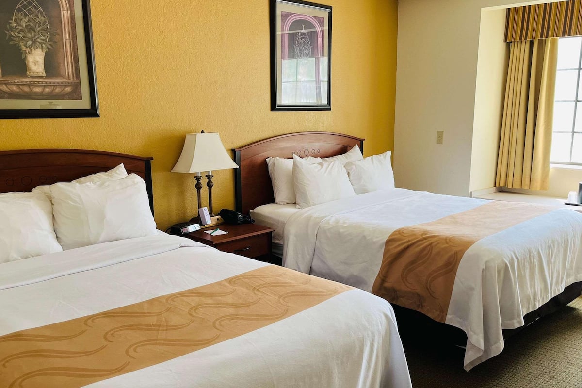 Une chambre d’hôtel avec deux lits, une table de chevet, une lampe et une fenêtre avec des rideaux.