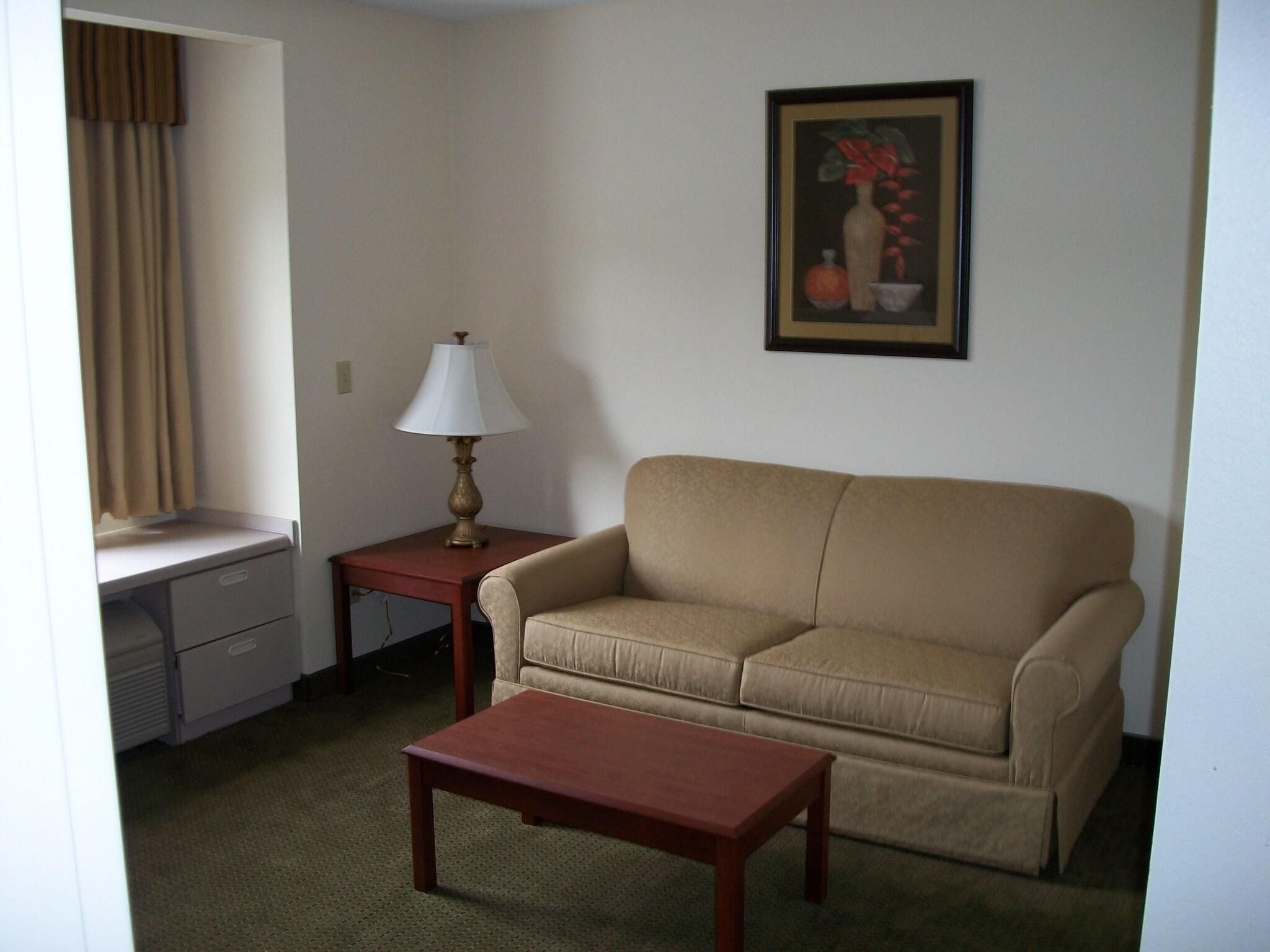 A living room with a sofa, a coffee table, a lamp, a desk with drawers, and a painting on the wall.