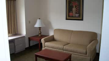 A living room with a sofa, a coffee table, a lamp, a desk with drawers, and a painting on the wall.
